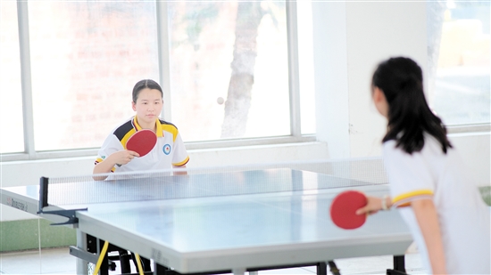 坐在轮椅上的陈敏霞（左一）在学校与同学切磋乒乓球。