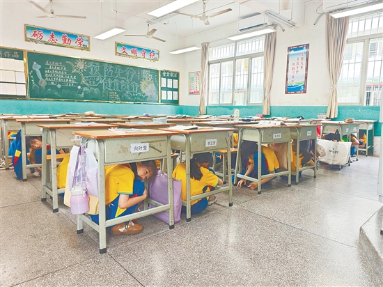 学生们双手抱头、蜷缩躲于课桌下方，规范避险。