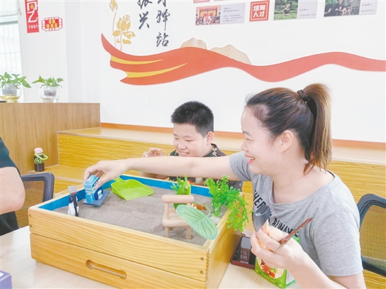 家长和孩子分别认真挑选沙具，专注地搭建场景、勾勒画面。